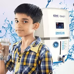 A small child drinking a glass of water with KENT RO in background