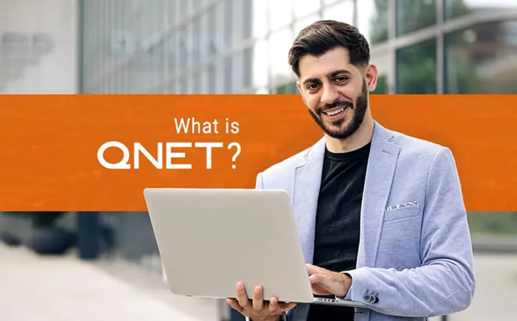 A businessman holding a laptop with "What is QNET?" written in the background