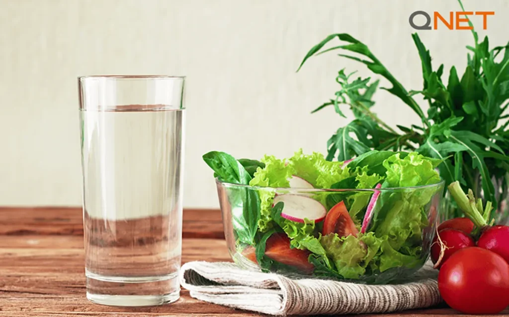 A glass of clean water on a kitchen counter surrounded by fruits & vegetables