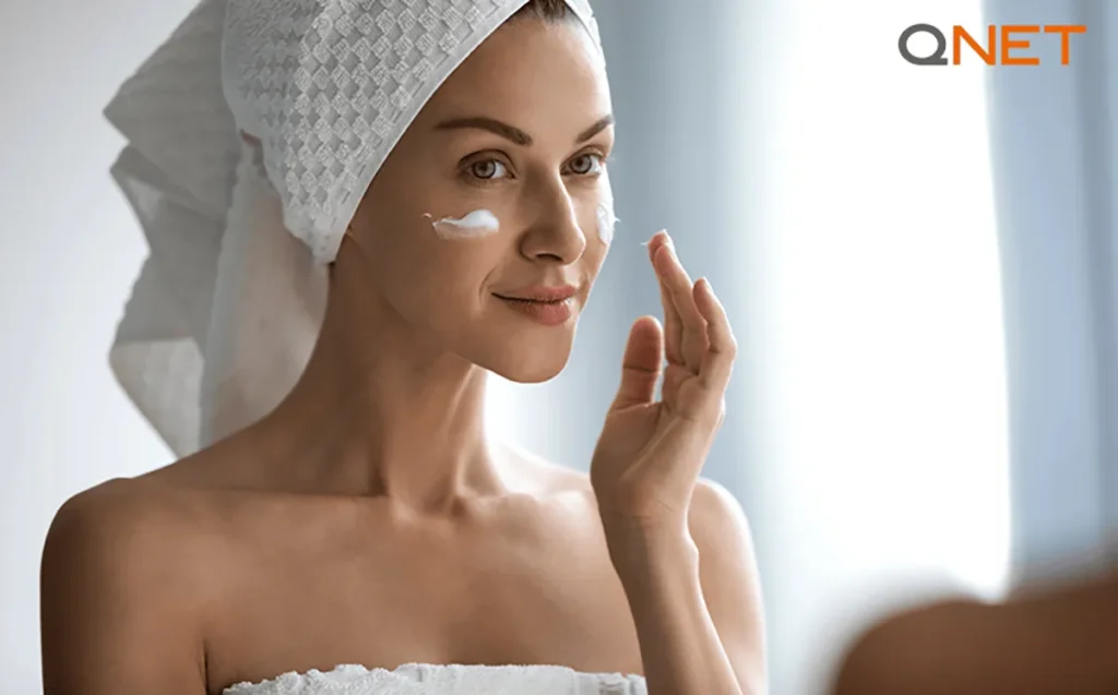 A woman looking into a mirror and applying face cream | Physio Radiance | QNET India