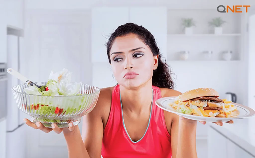 A young Indian woman managing her diet with a plate of junk food in one hand and healthy food in the other