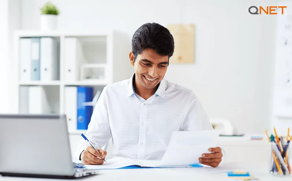 A young QNET entrepreneur writing on a document in his office