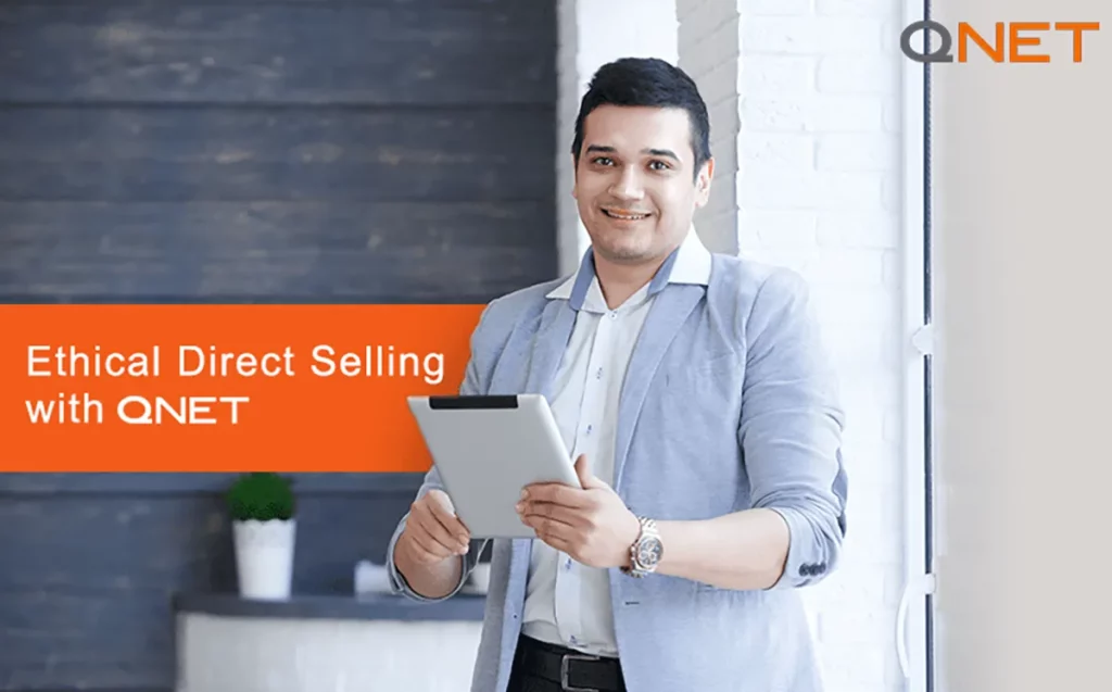 An ethical QNET direct seller smiling while standing indoor with a tablet in his hand